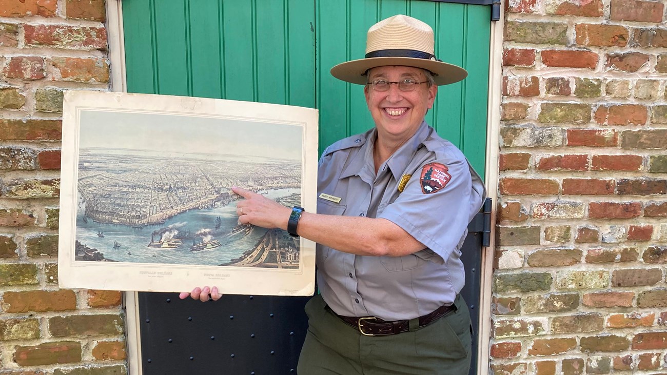 Ranger Karen in a flat hat holding a historic painting of new orleans