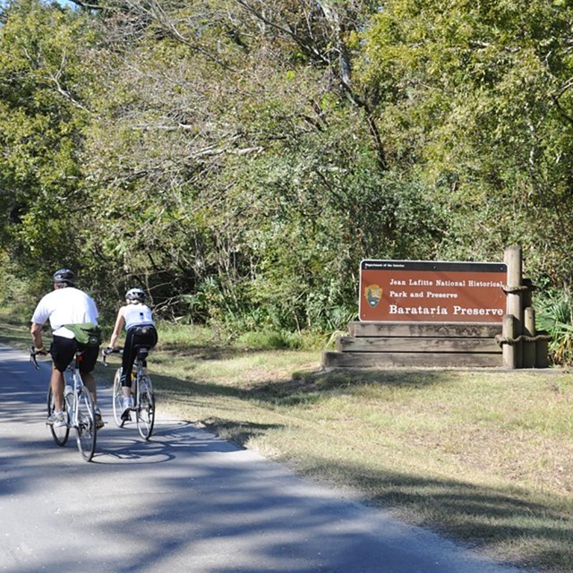 Bicyclists ride by the Barataria Preserve sign