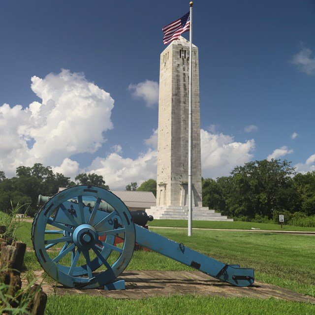 A cannon faces the battlefield in front of the Chalmette Monument and an American flag