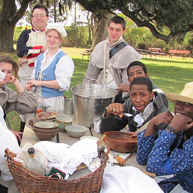 a group of reenactors dressed in period dress around a picnic table