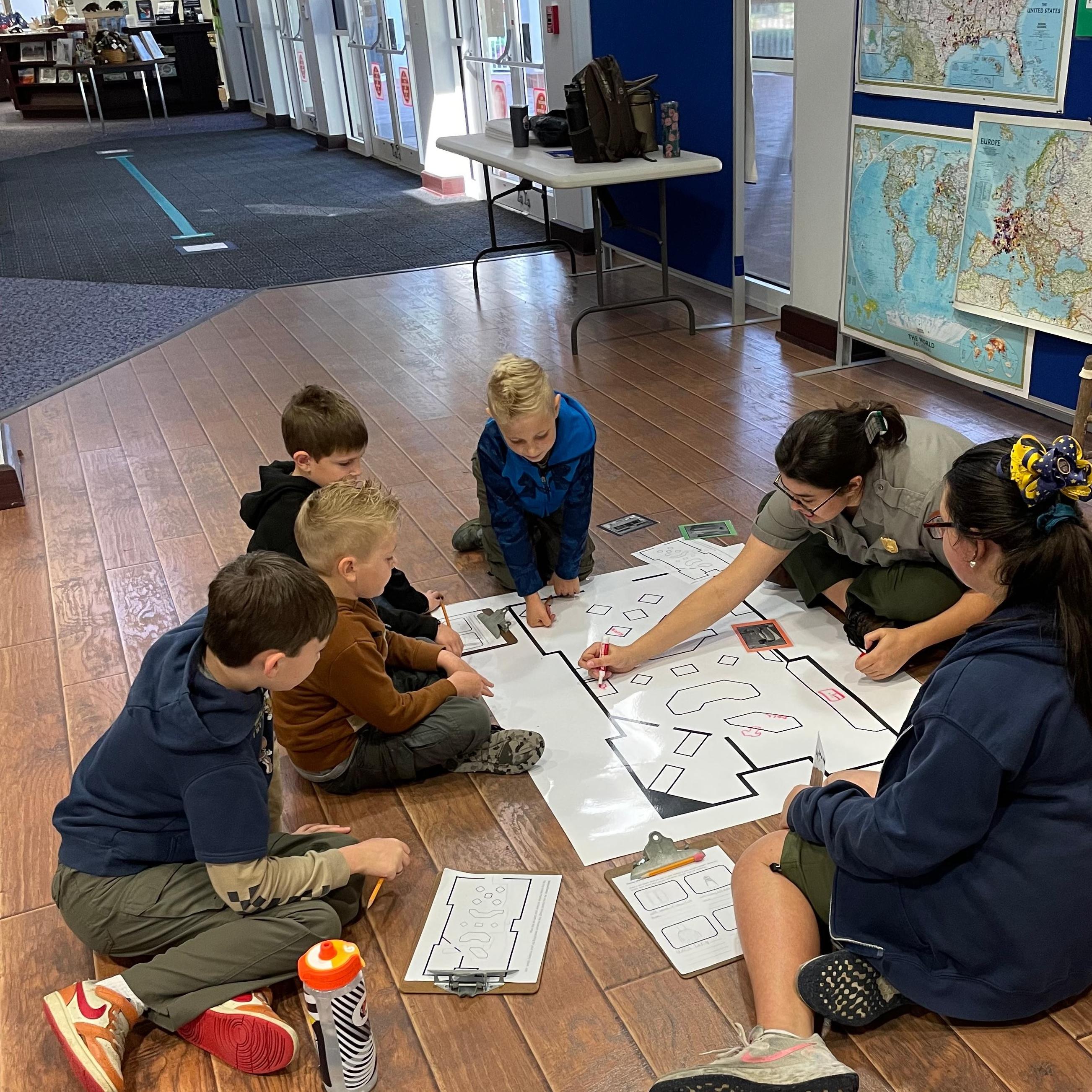 A ranger and cub scouts surround a map on the ground.