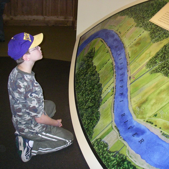 Boy kneels in front of big map of Mississippi River