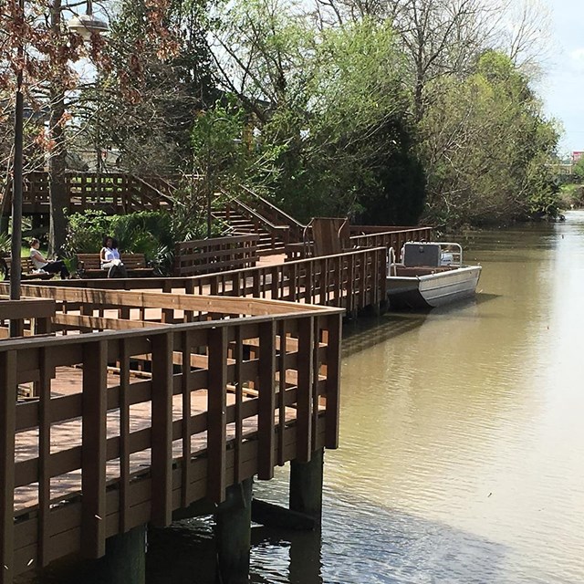 Deck with people on it next to a wide tree-lined waterway