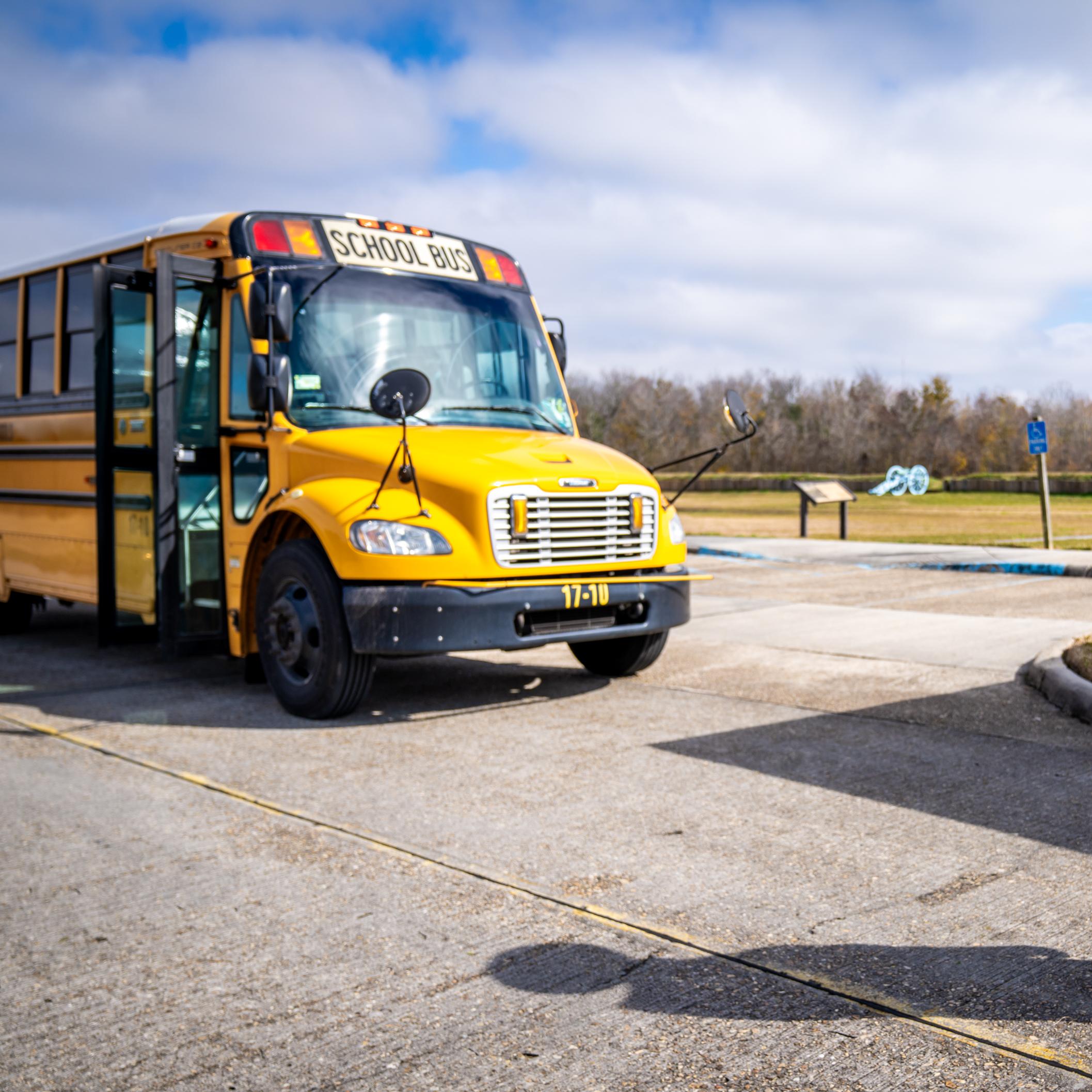 A school bus with a park ranger in a safety vest in front of it.