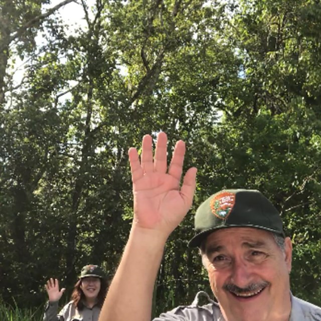 a ranger on a trail waving hello