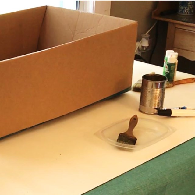 cardboard box on table with paints, can of water, and a brush in a tray