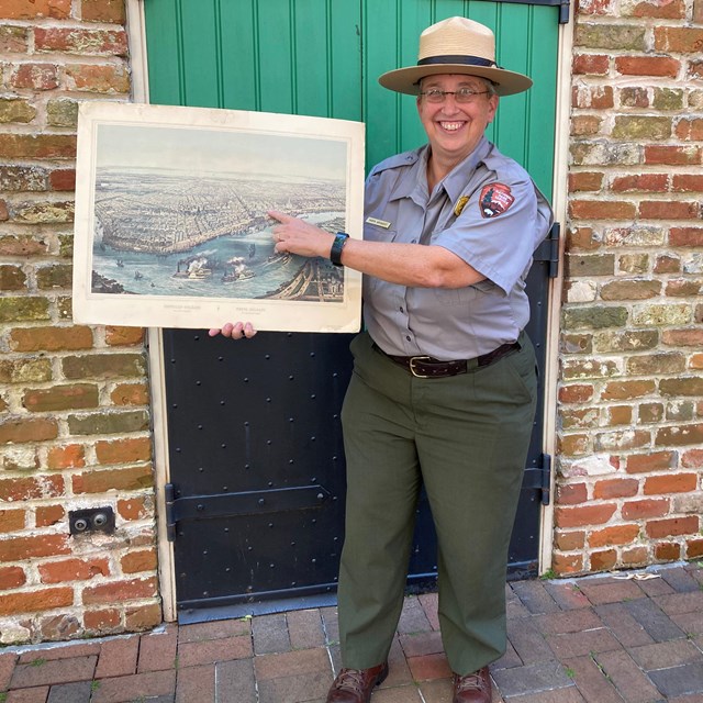 Ranger Karen in a flat hat holding a historic painting of new orleans