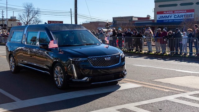 Hearse driving past people gathered on street