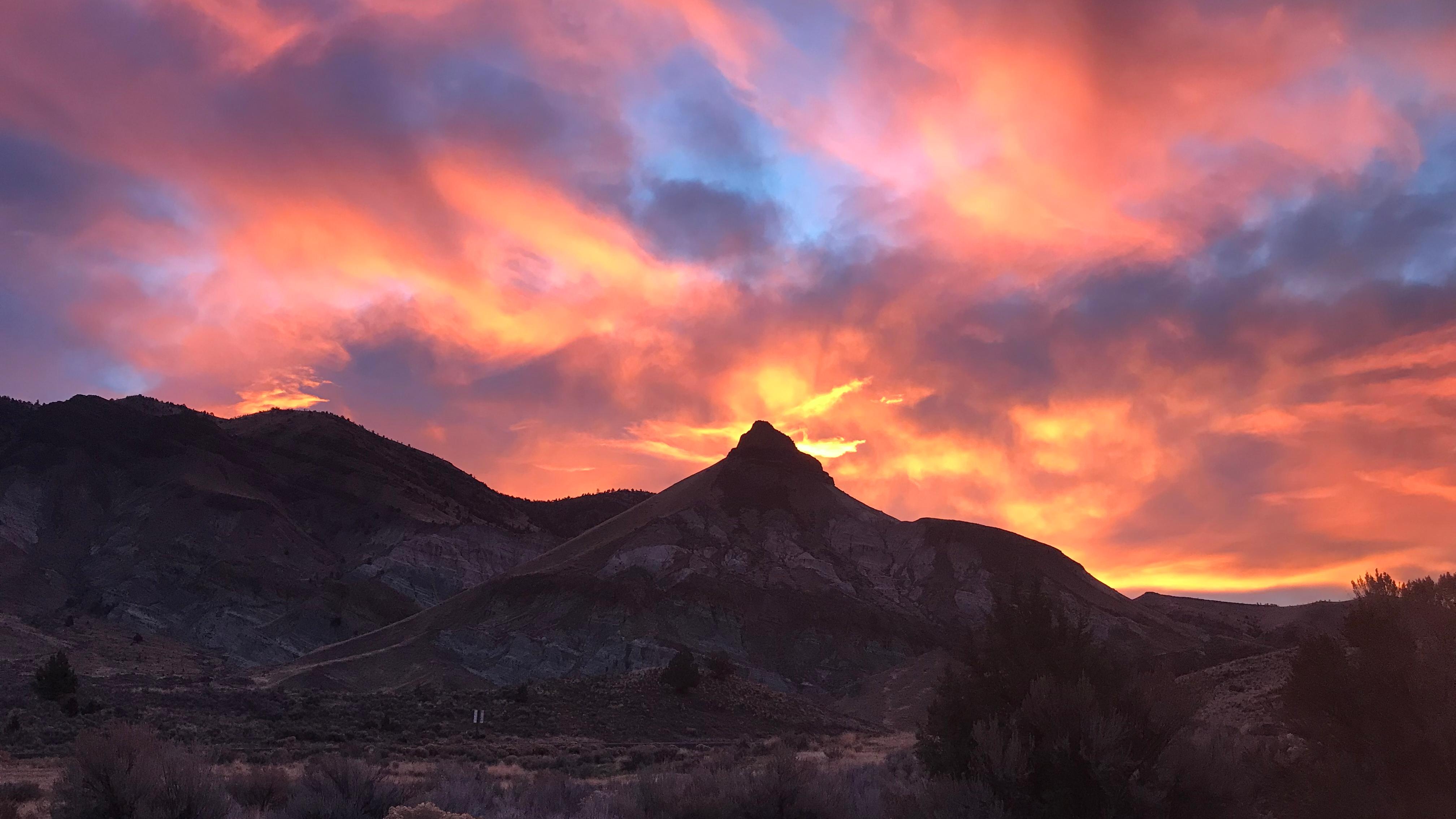 A pointed hill in shadow with pink and orange clouds of sunset above.