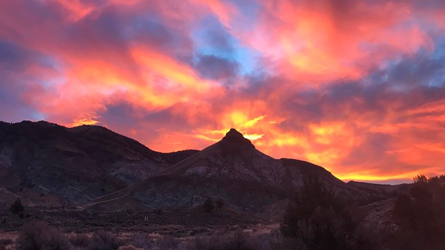 A pointed hill in shadow with pink and orange clouds of sunset above.