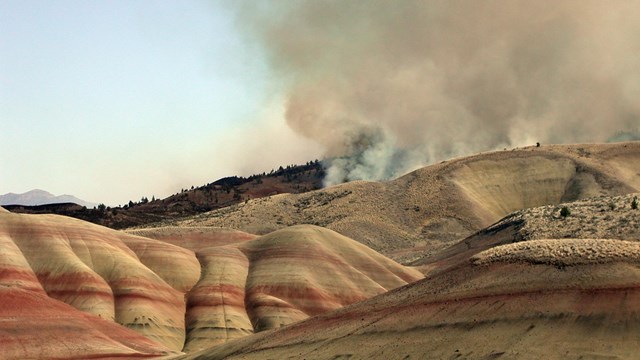 Smoke billows up from behind yellow and red stripped hills.