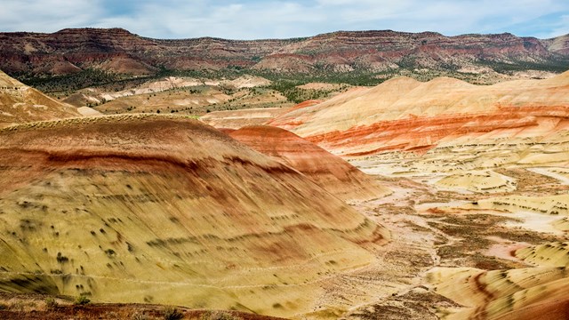 Red and yellow striped hills with a basalt ridge and cloudy blue skies in the background.