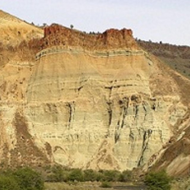 Layered rock made up of blue-green claystones with a layer of reddish-brown ignimbrite on top.