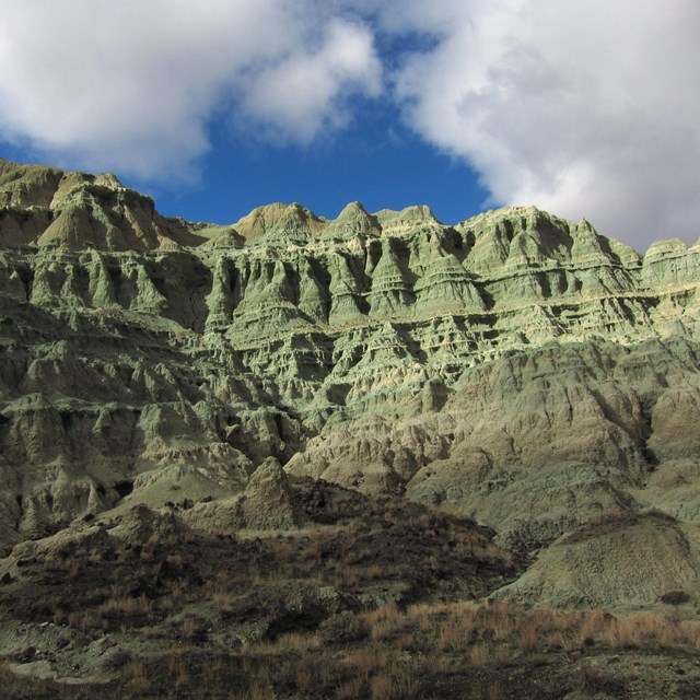 Hills of layered rock made up of blue-green claystones that has eroded into spires.