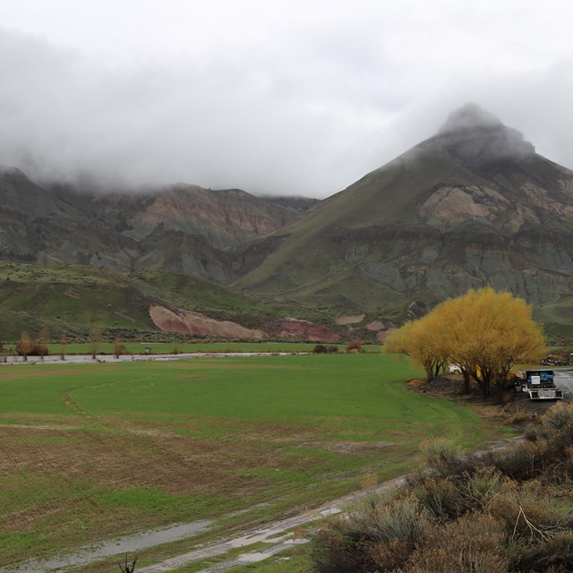 Clouds partially covering a hillside including a pyramid-shaped hill. A river runs below.