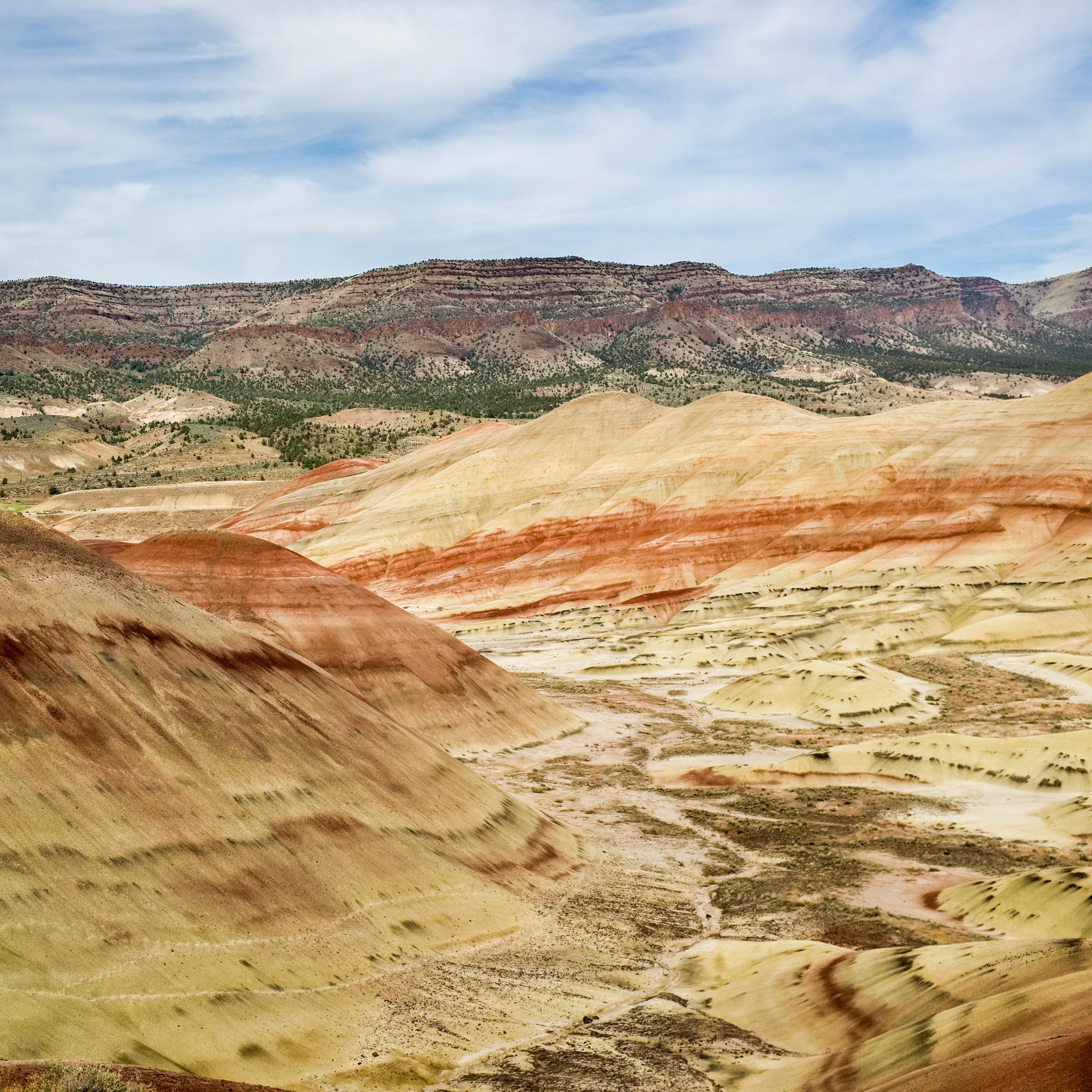 Red and yellow striped hills with a basalt ridge and cloudy blue skies in the background.