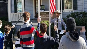A uniformed Park Ranger performs a Junior Ranger swearing-in ceremony in front of the JFK Birthplace