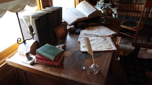 Looking down on John Muir's desk. Piles of books, papers and an old quill pen. 
