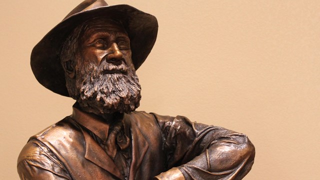Bronze statue of an older John Muir wearing a hat and resting his arm on a stick.