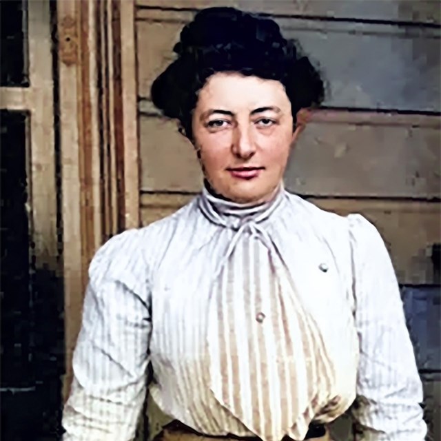 A younger woman in a nice dress is sitting on the porch and posing for the camera. 