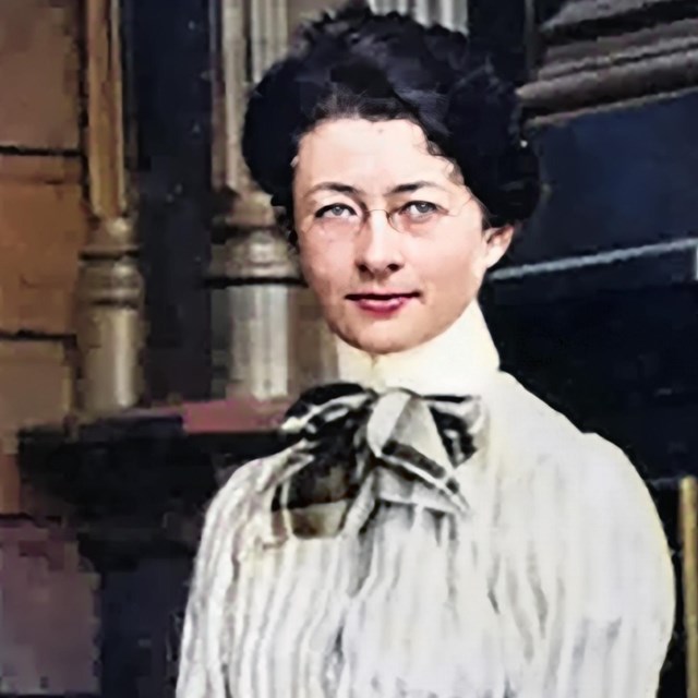 A younger woman in a nice dress is sitting on the porch and posing for the camera. 