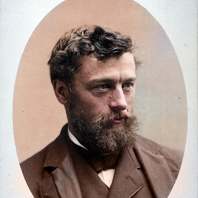 A middle-aged man with a long beard and wearing a suit is posing for the camera. 