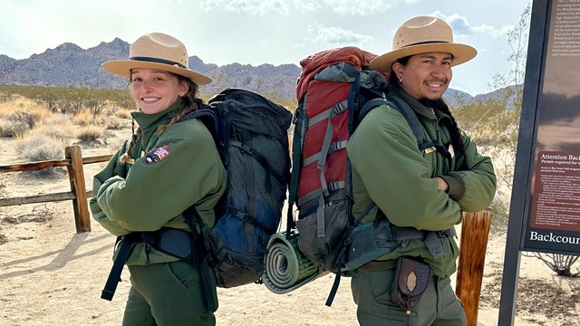 Two rangers wearing large backpacks and standing back to back to each other