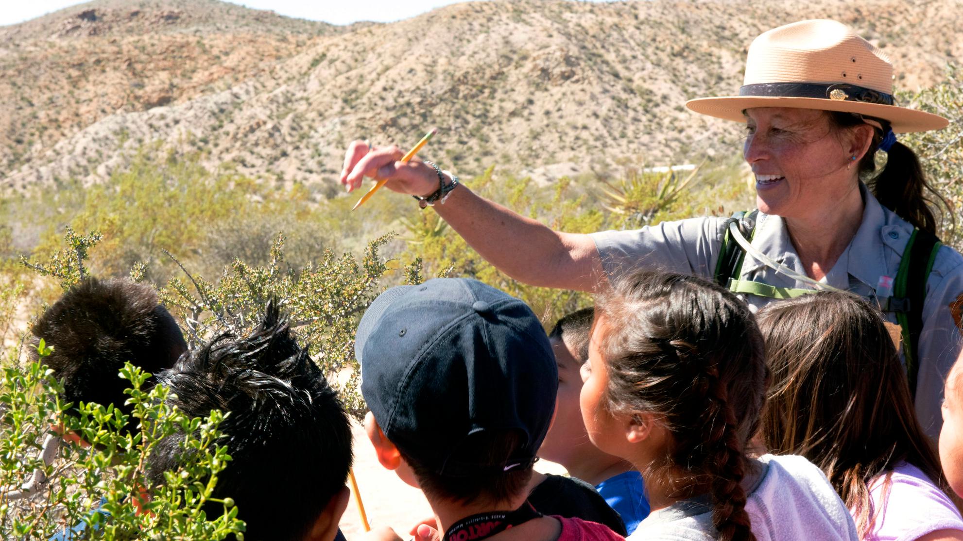 A ranger and kids surrounded by desert vegetation. 