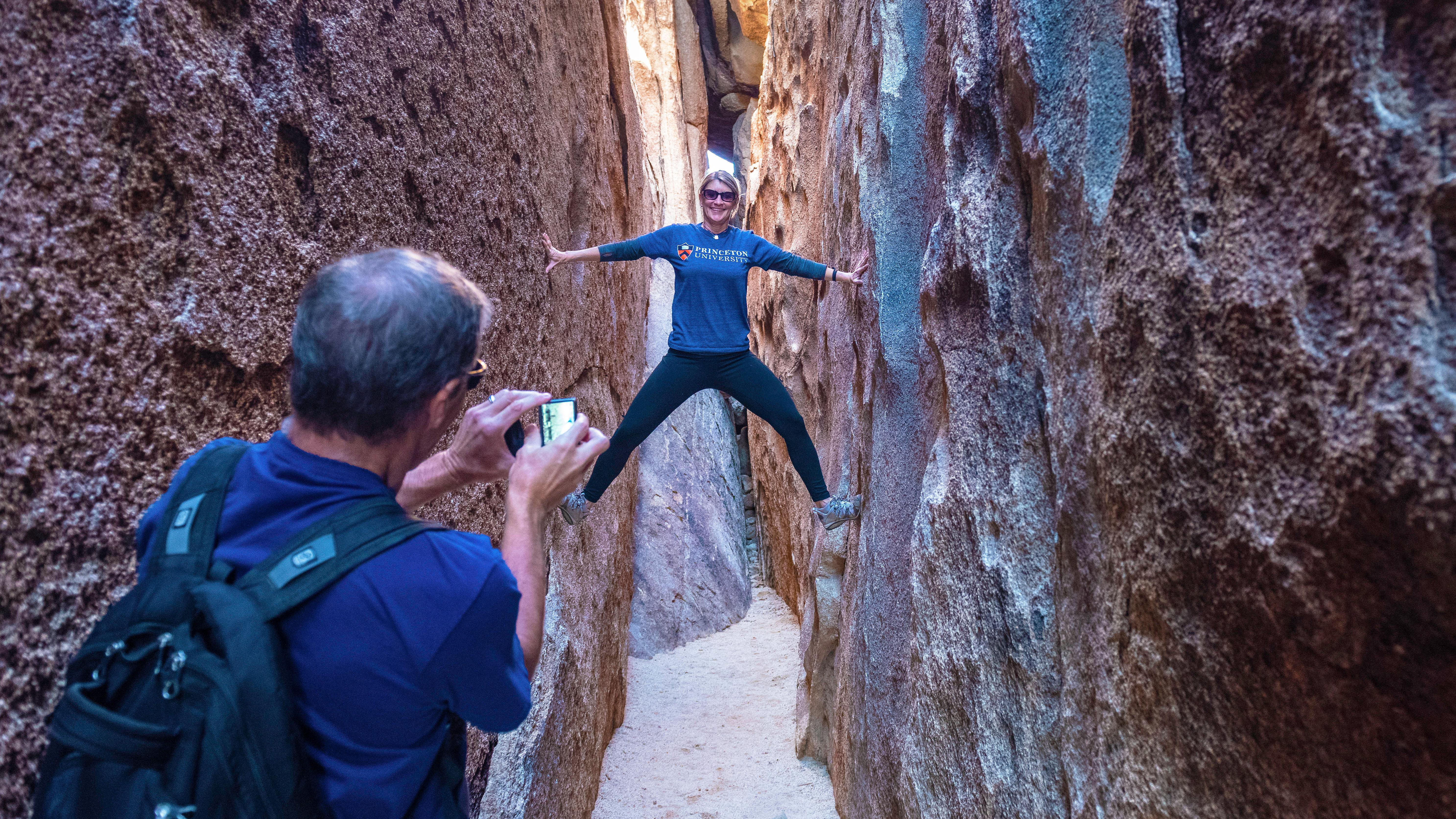 A woman poses for a photo and braces against the sides of a slot canyon.