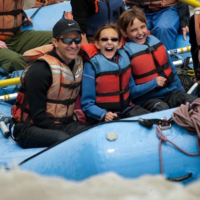 A group of adults and children raft on a river in wilderness.