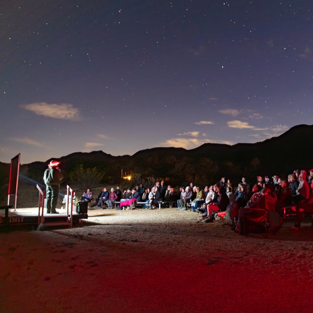 Rangers with red lights talk in front of a large audience, with the stars behind