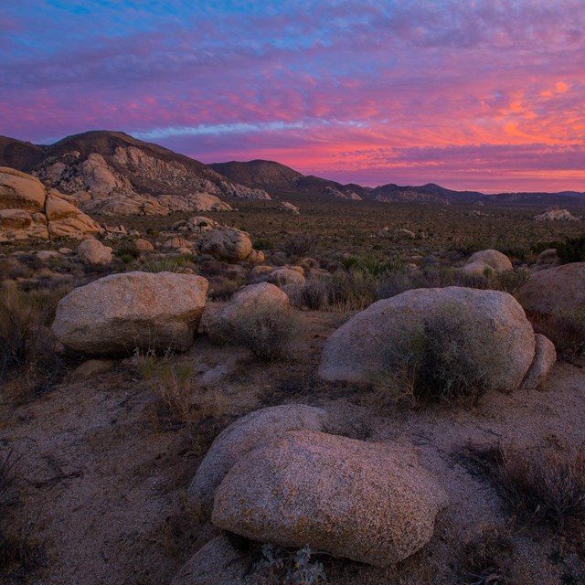 Color photo of vibrant sunset colors in the clouds with monzogranite boulders in the foreground.