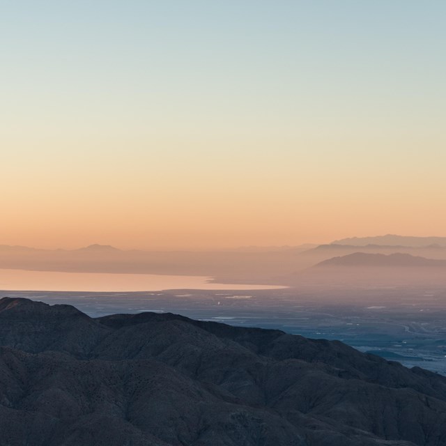 Color photo of sunrise as seen from Keys View looking out over the Salton Sea. It is very hazy/pink.