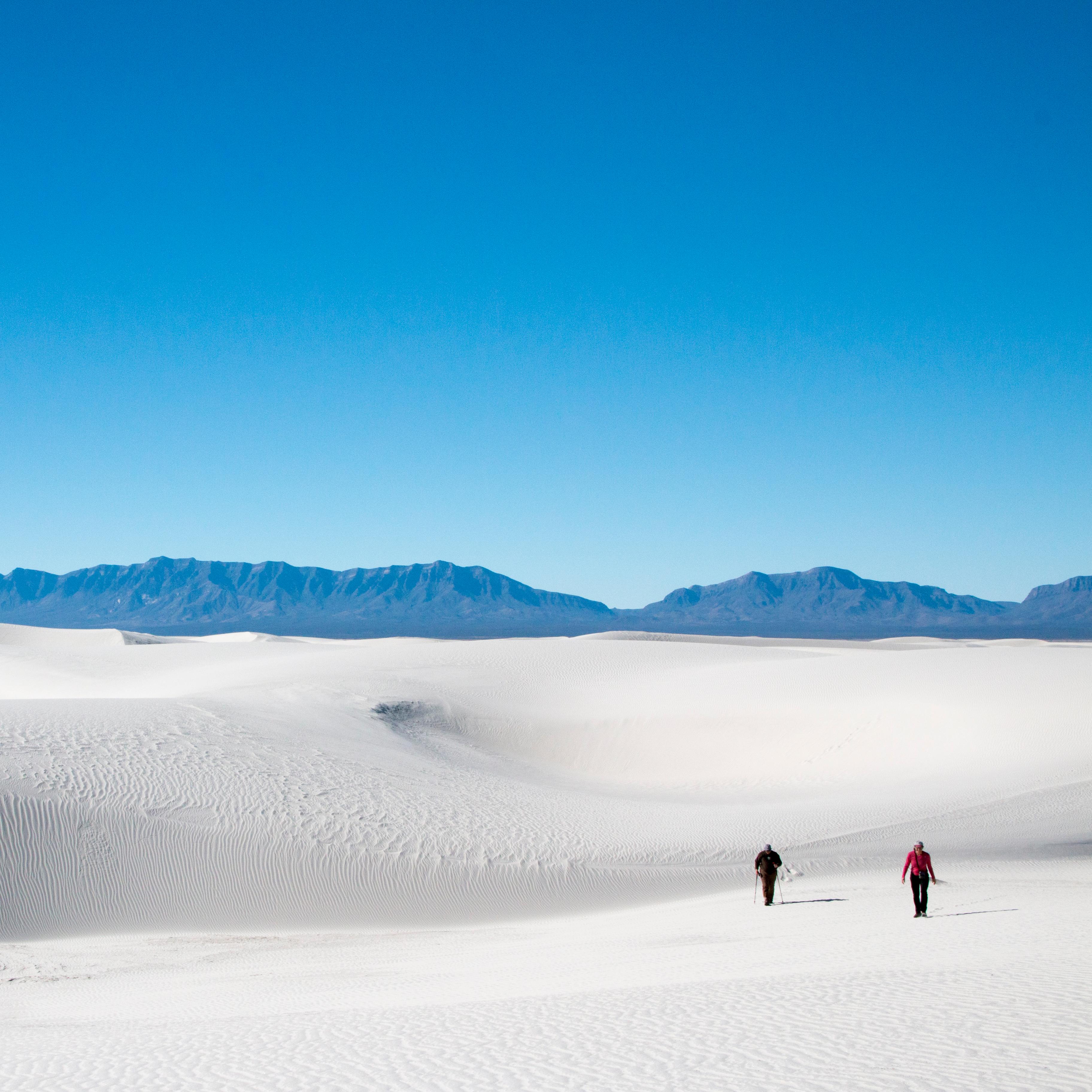 Two people walking across white sand dunes