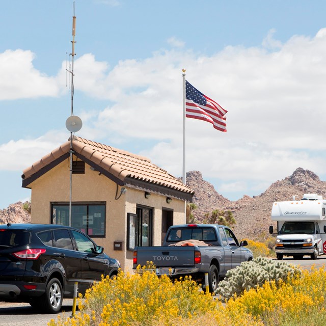 A small, peak-roofed building with an American flag and cars passing by