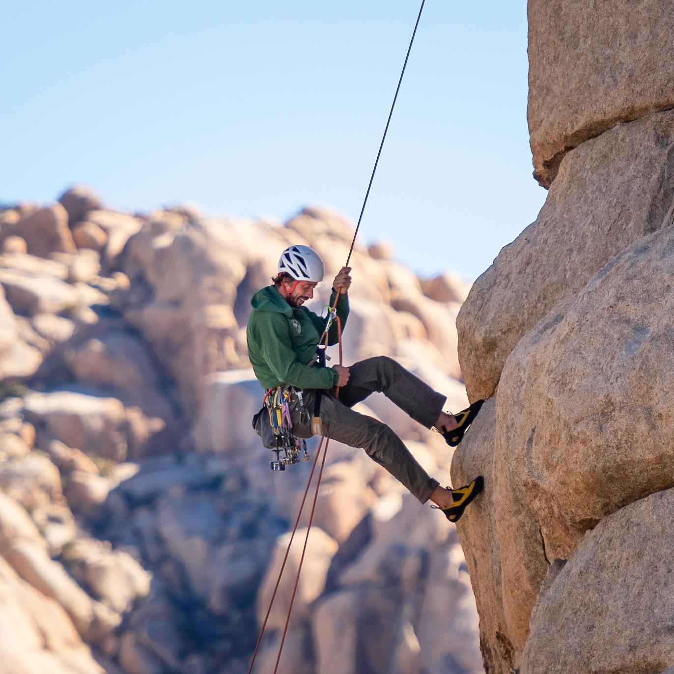  A climber steward in a green uniform shirt rappels down a climbing route.