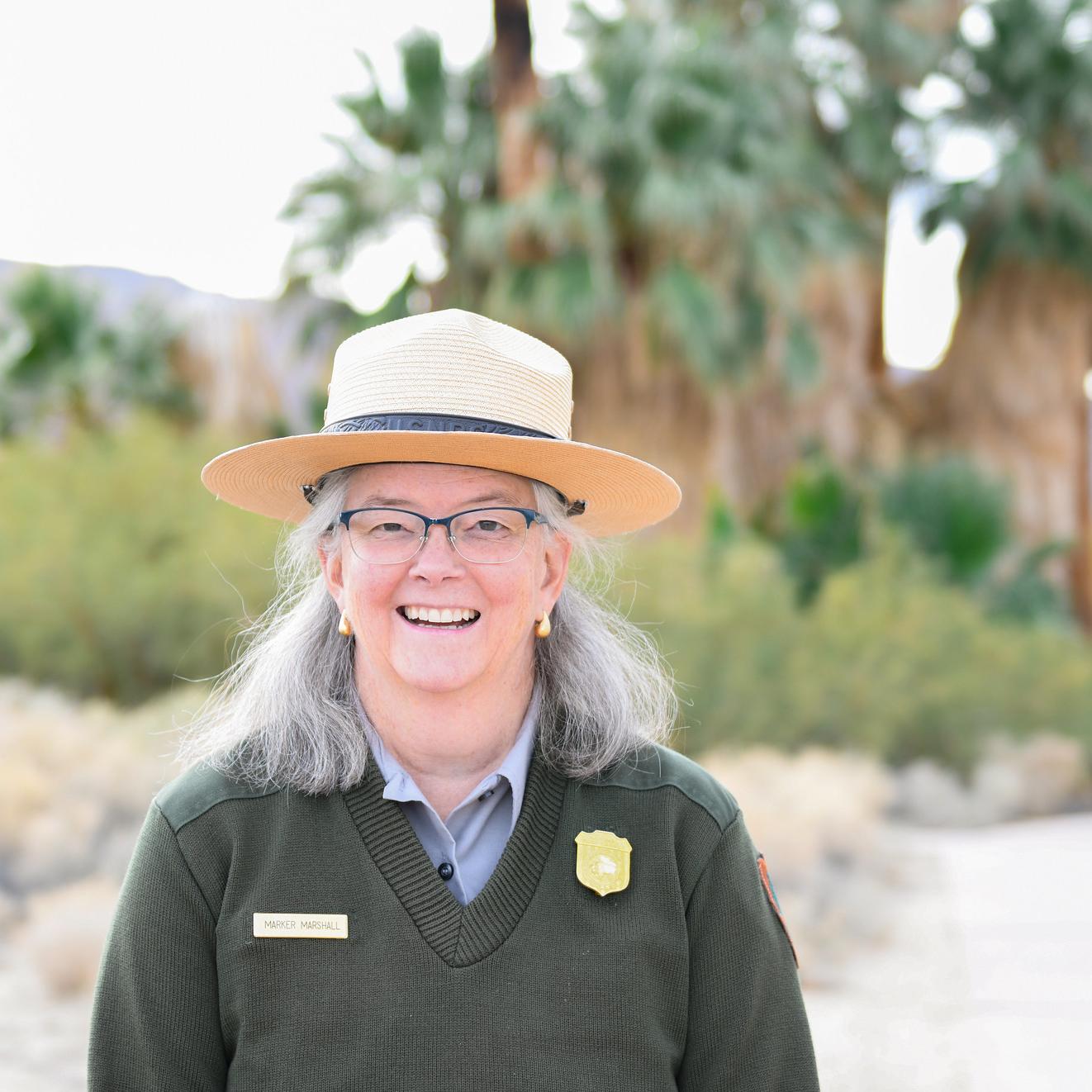 A ranger stands in front of palm trees and smiles at the camera