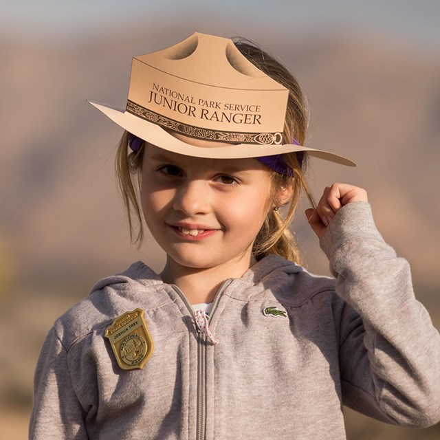 A Junior Ranger stands smiling with their hat and badge. 
