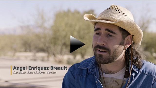 A screenshot of a bearded man wearing a cowboy hat speaking with lower thirds and a play button