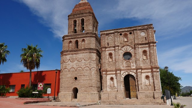 A three-story brick church with a large bell tower on the left and an arched wooden door