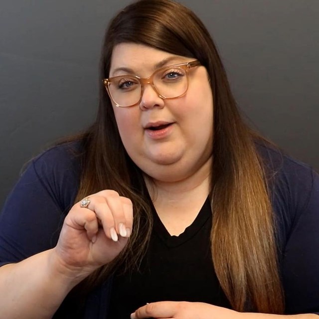 A woman with long hair and glasses signs in ASL