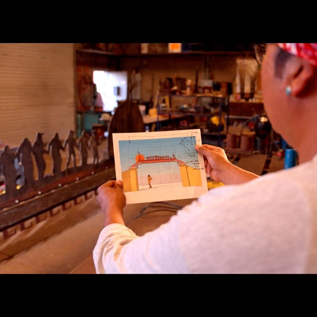 A man holds an image of an archway while the metal sculpture depicted sits in front of him