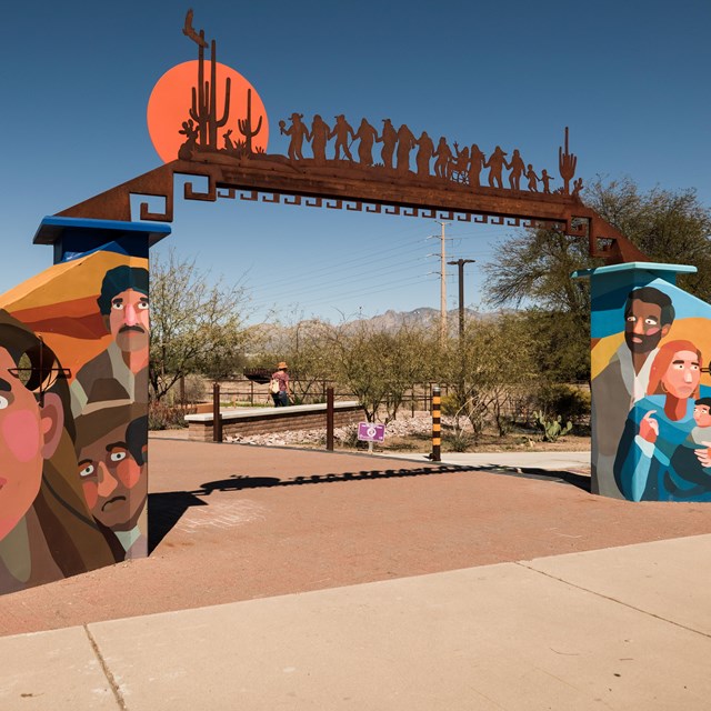 The colorful entrance to the Anza Trail Cultural History park shows a painted mural &metal sculpture