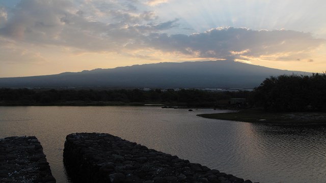Makaha gate and fishpond wall with the sun rising over volcano in the background