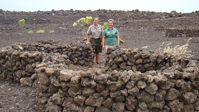 Two park employees standing next to a large planter made of lava rock