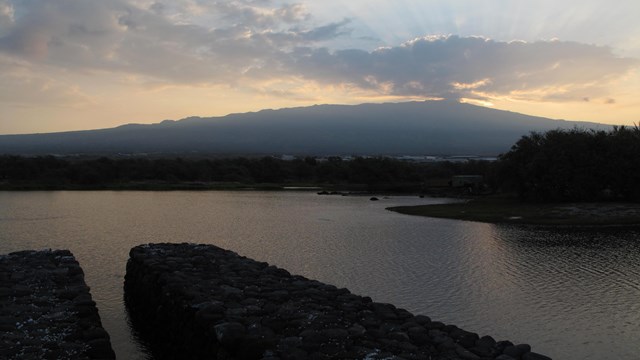 Makaha gate and fishpond wall with the sun rising over volcano in the background