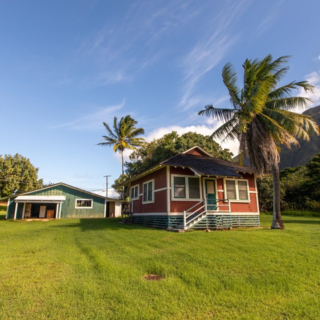 A red building and blue building stand on a lawn with a few trees nearby. 