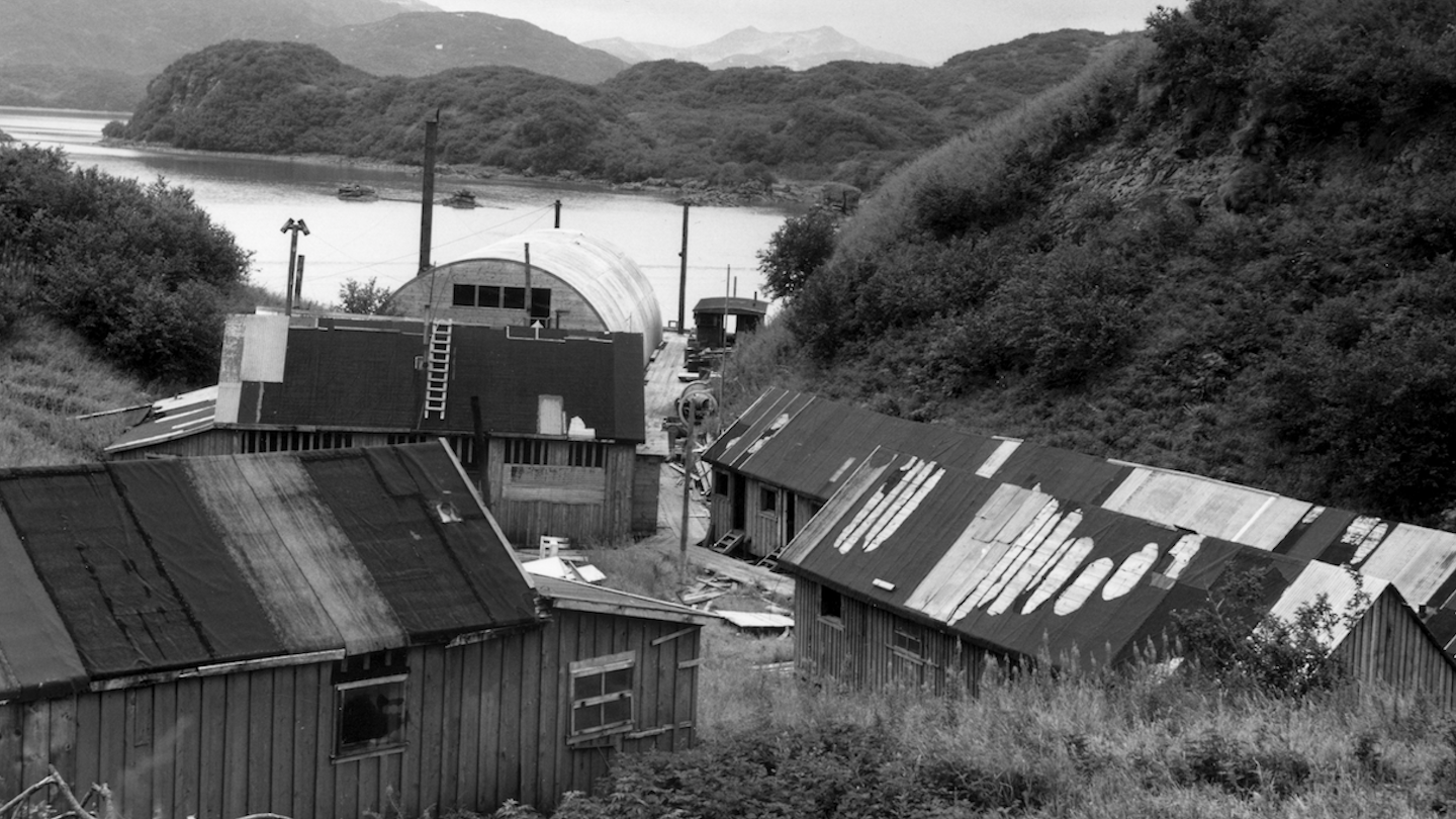 A black and white photograph of a collection of cannery buildings by a bay.