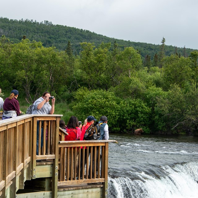a group of people standing on a wooden platform next to a waterfall