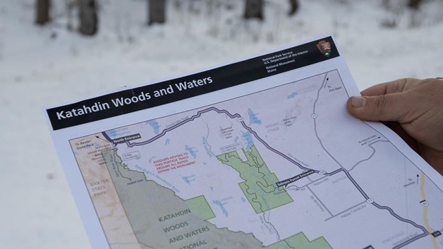 A visitor holds a monument map in their hands against a snowy backdrop.